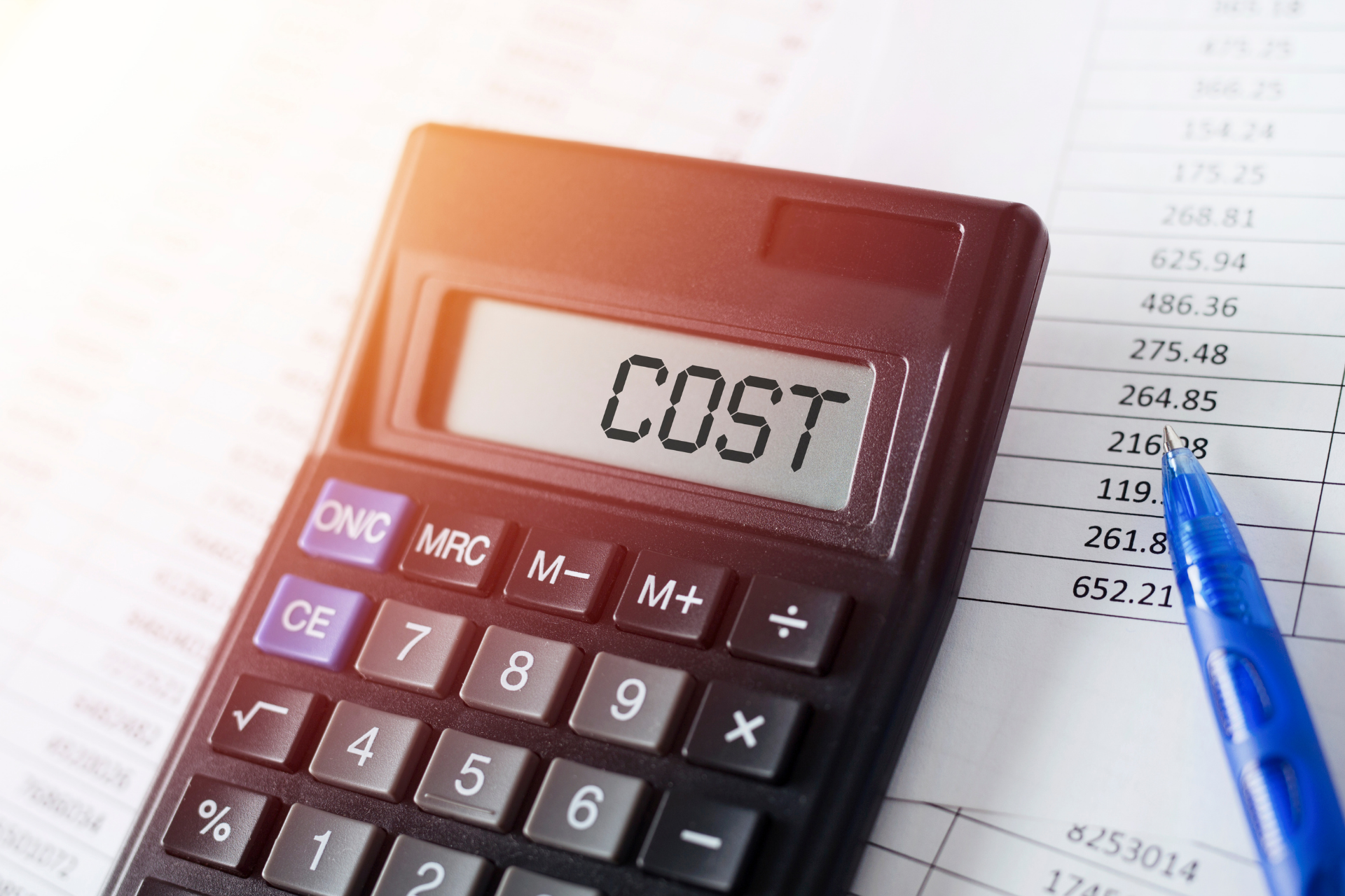 Calculator showing “COST” beside a blue pen and financial paper with numbers.