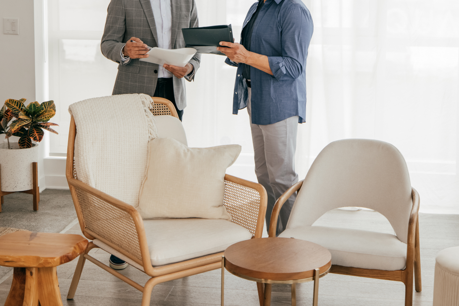 Two people discussing paperwork in a bright living room with cream armchairs and small wooden tables