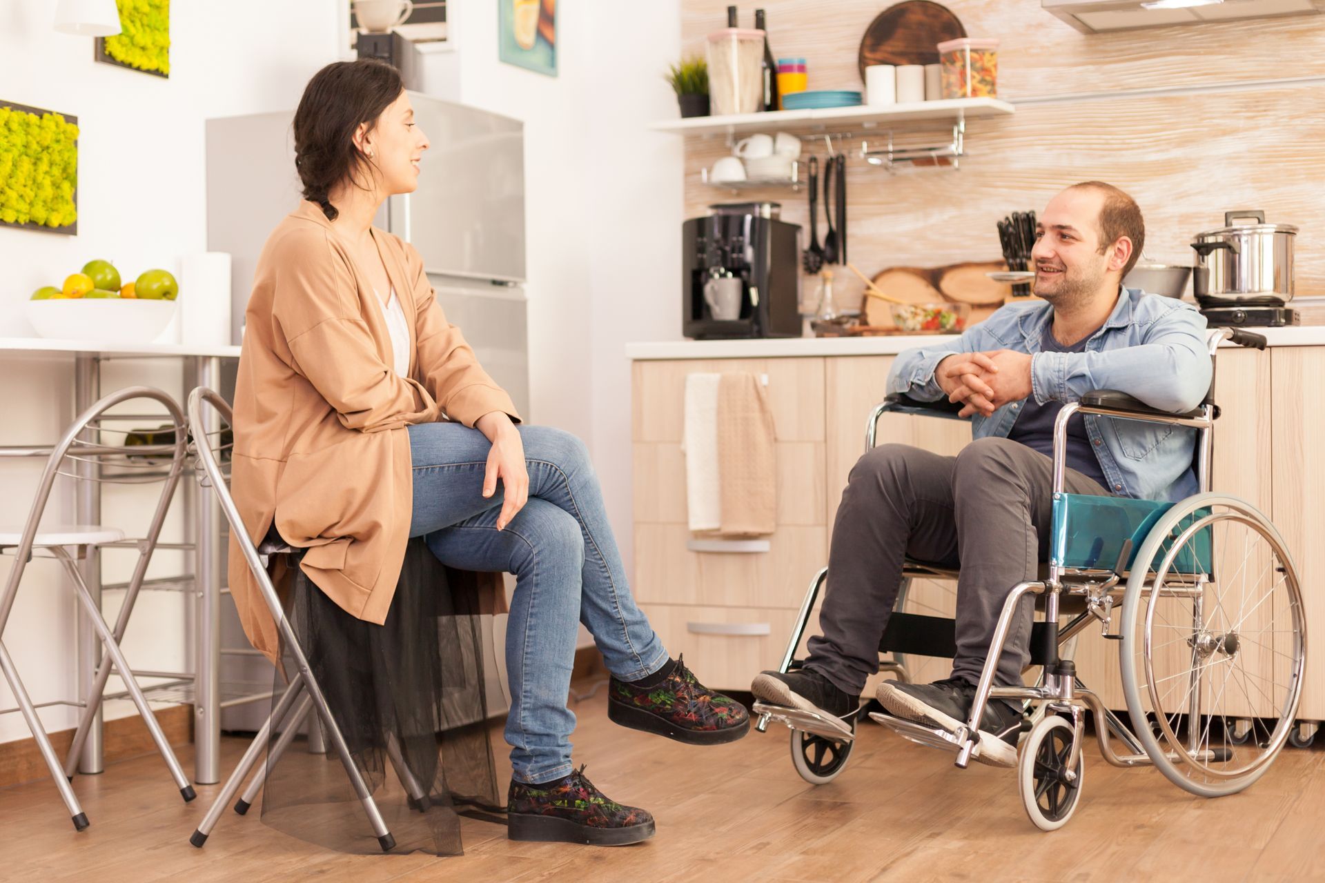 Woman sitting, conversing with a person in a wheelchair in a kitchen.