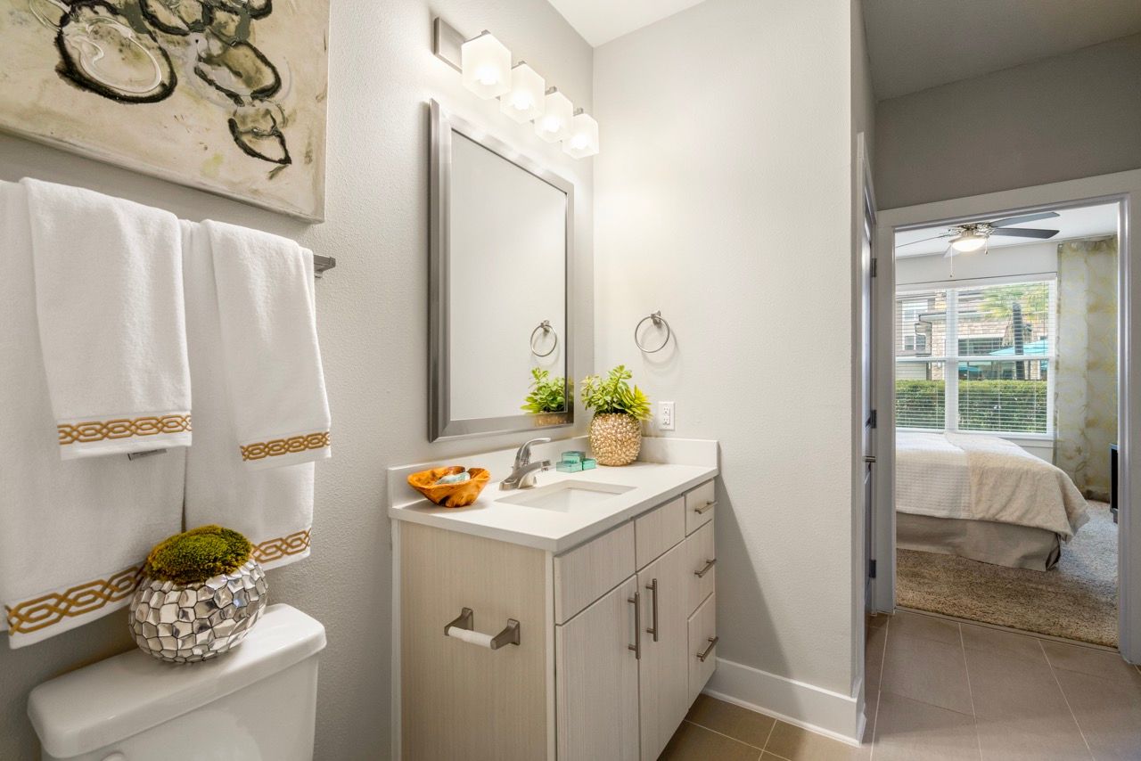 Bathroom vanity with sink, mirror, and towels; doorway to a bedroom visible in the background.