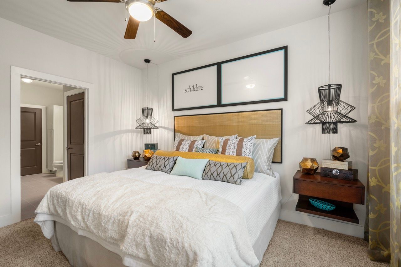 Bright bedroom with a large bed, plush bedding, two nightstands, and a ceiling fan.