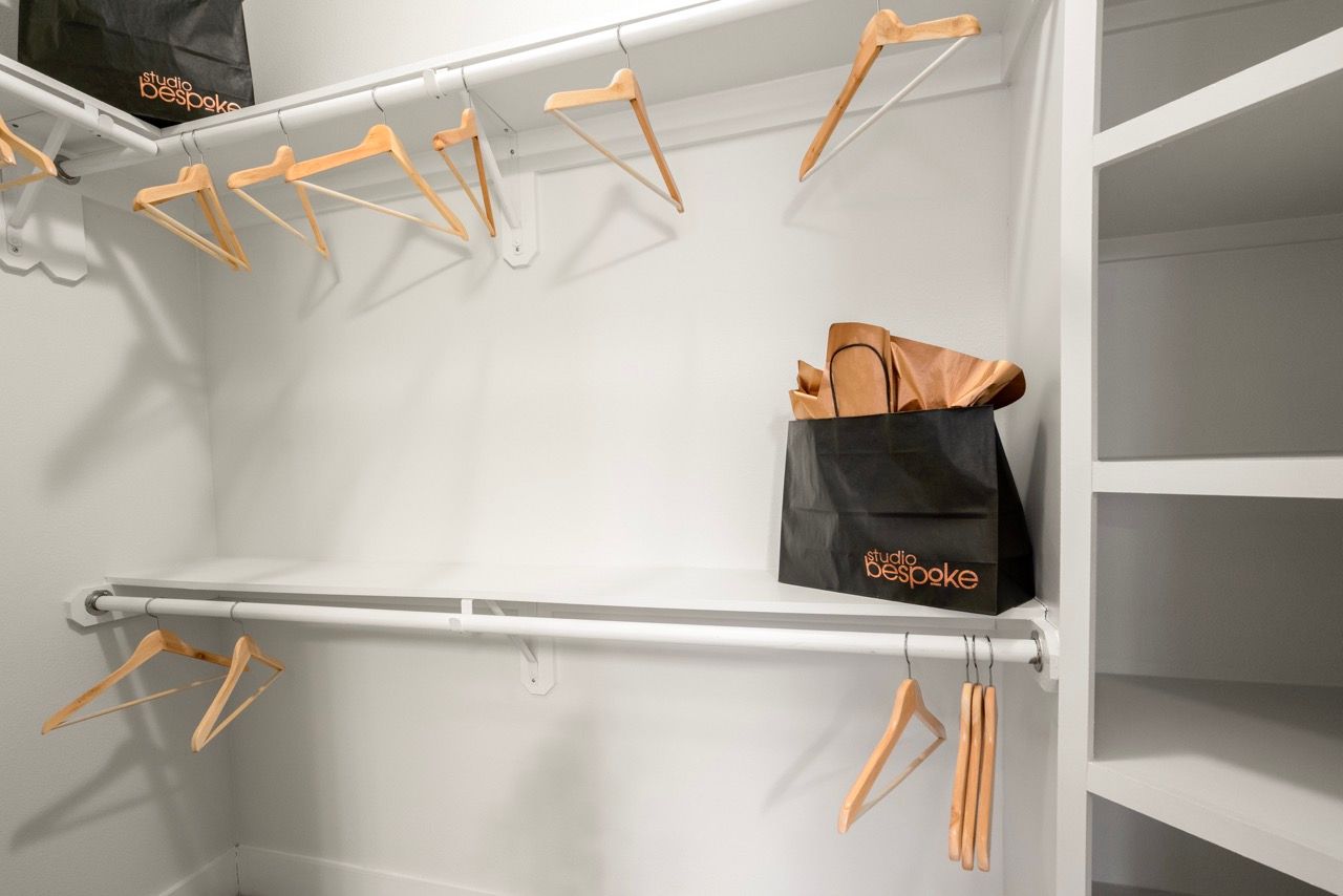 Walk-in closet with white shelving, wooden hangers, and a black Studio Bespoke bag on the shelf.