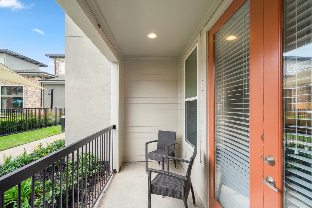 Balcony with two wicker chairs, an orange-framed door, and blinds in a modern apartment.