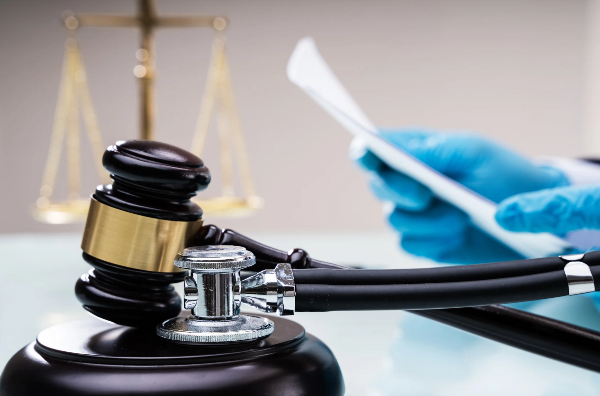 Gavel and stethoscope on table with law scales, a person holding paper, gloves.