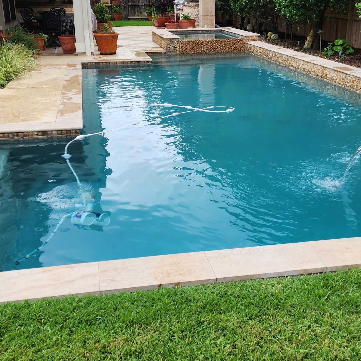 Swimming pool with turquoise water, a hot tub, and tan tile surrounds; lush green grass in the foreground.