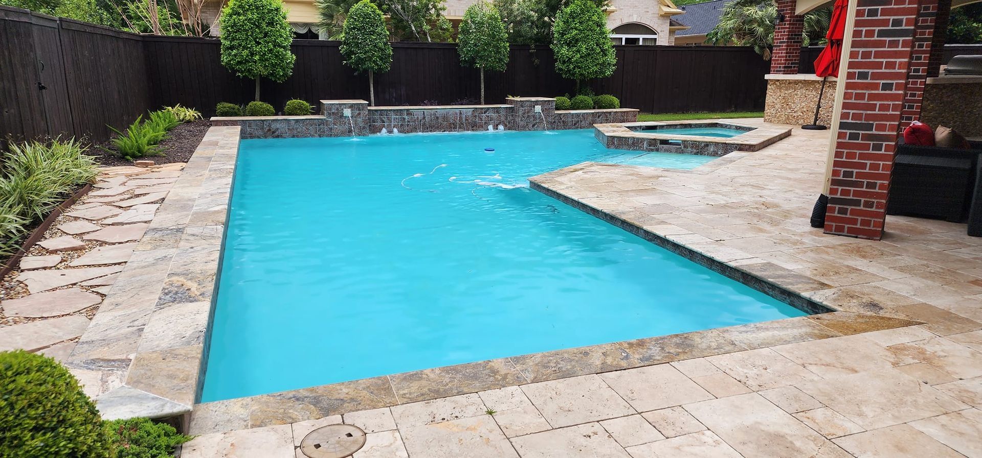 A backyard swimming pool with a hot tub and waterfall feature. Brick columns and paving surround the pool.
