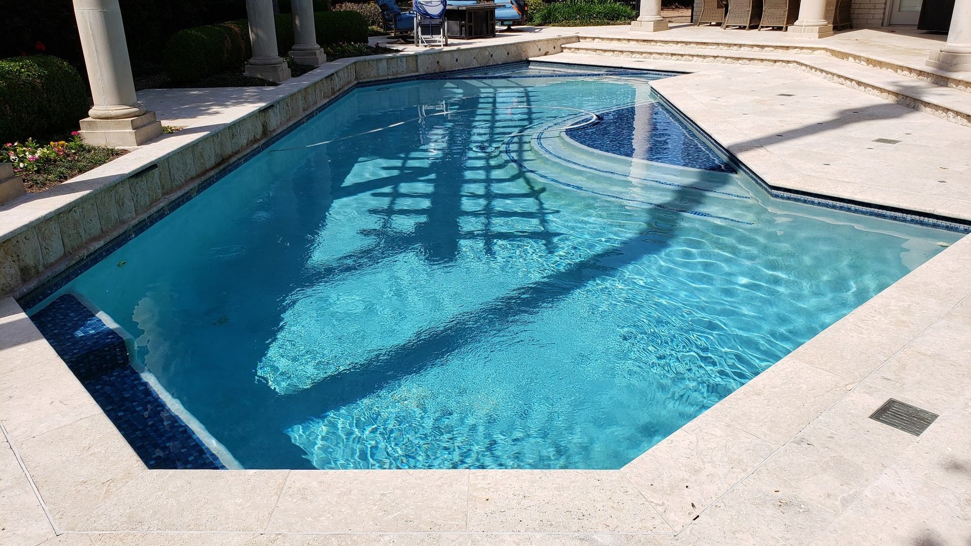 Swimming pool with blue water and tiled edges, surrounded by stone patio.