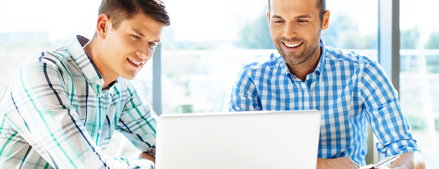 Two men are sitting at a table looking at a laptop computer.