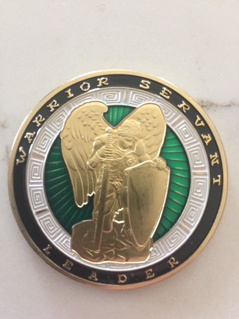 Challenge coin with a kneeling, golden-winged figure, angel or warrior, holding a sword and shield on a green background.  