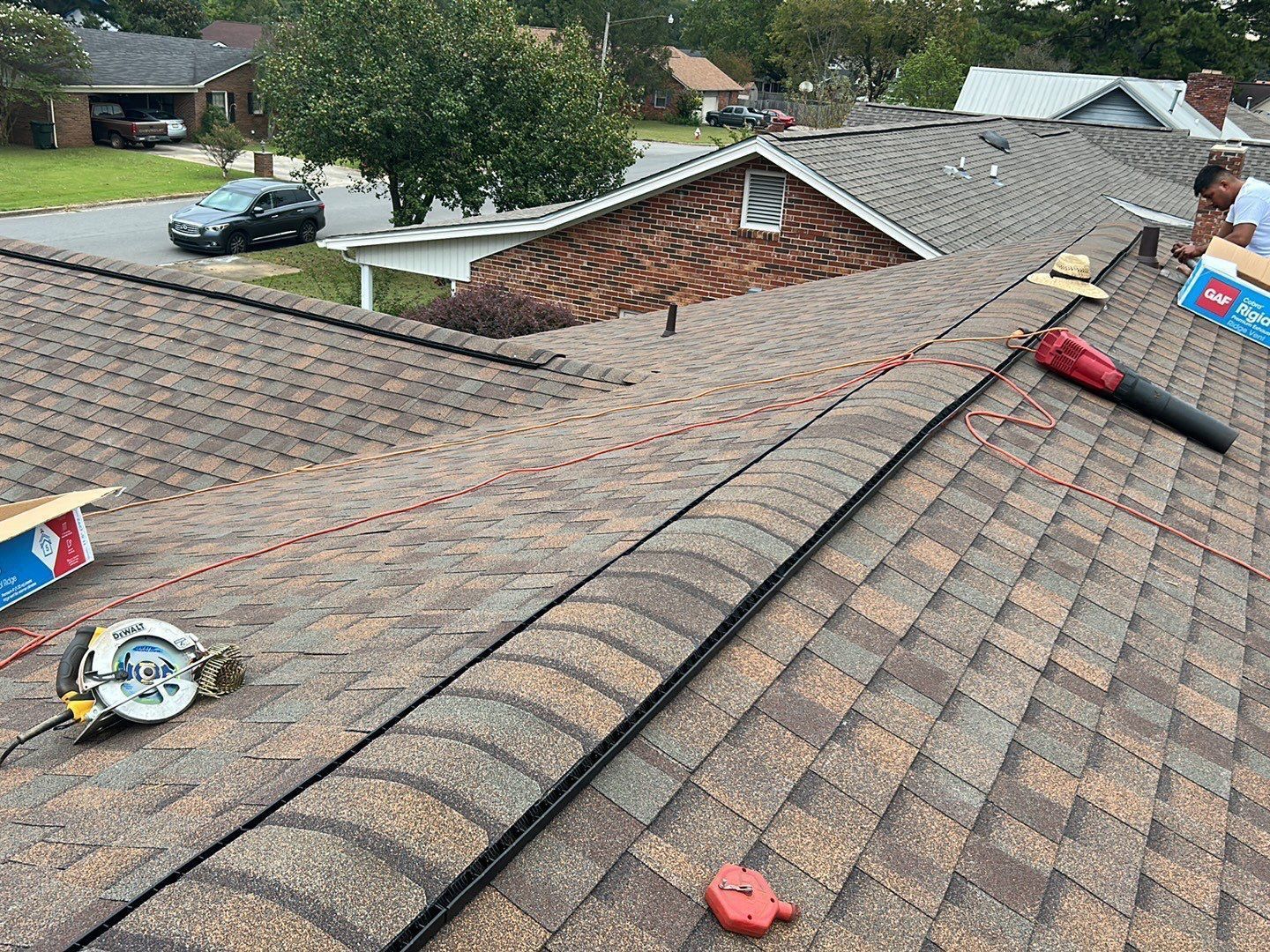 Workers repairing a brown shingled roof. Tools, including a circular saw and blower, are present.