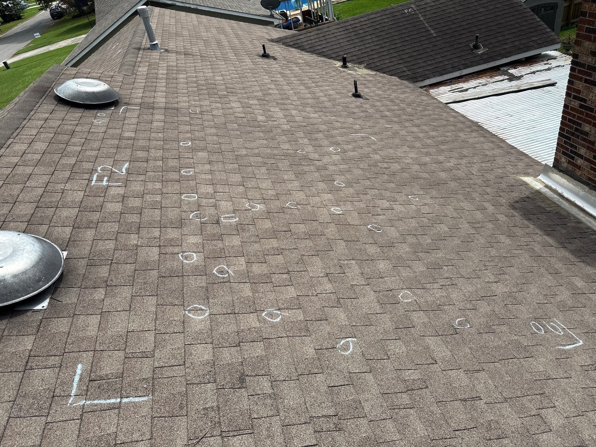 Close-up of a dark gray asphalt shingle roof on a house, with a blue sky visible above.
