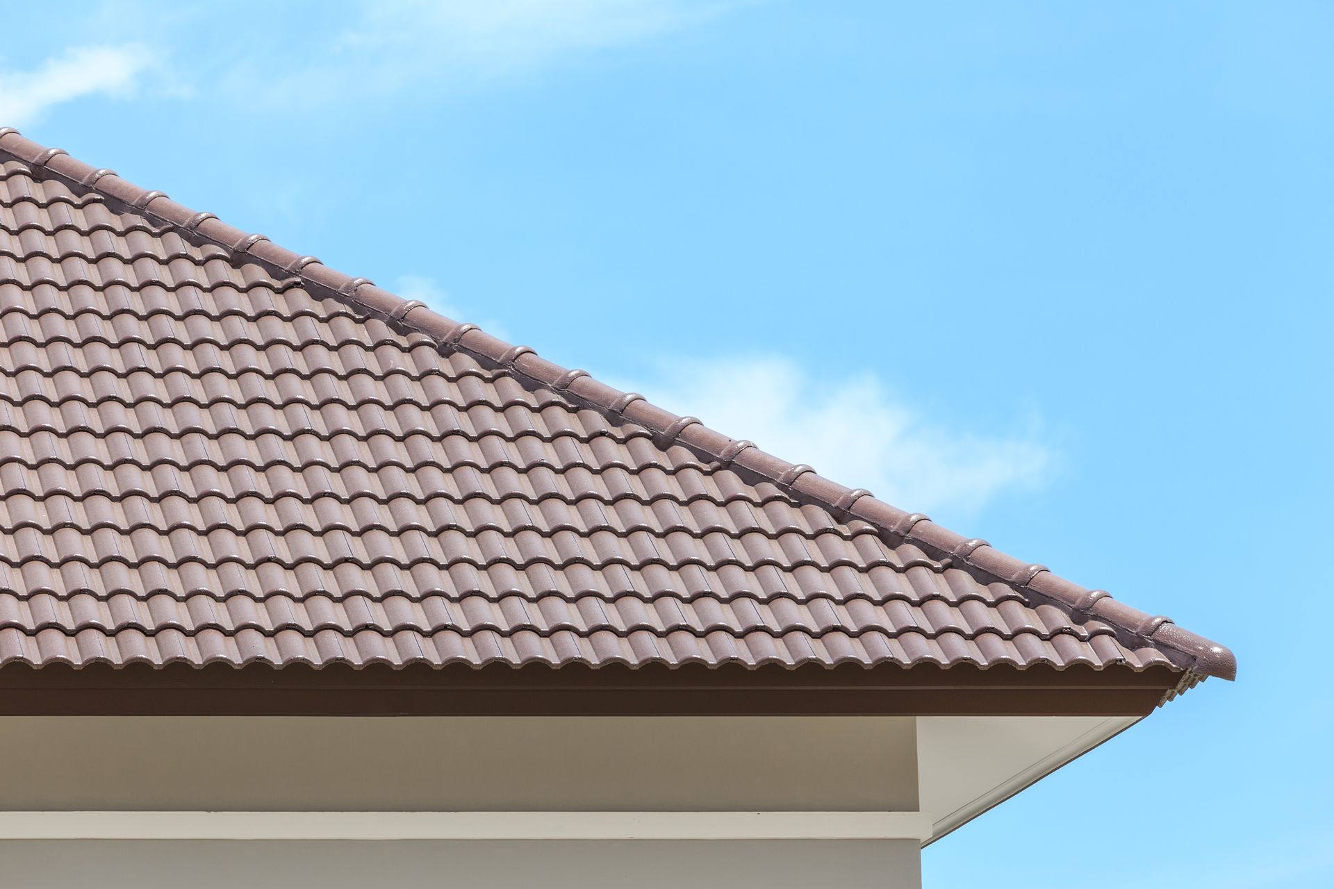 Brown tiled house roof under blue sky with clouds, showcasing durable residential roofing design.