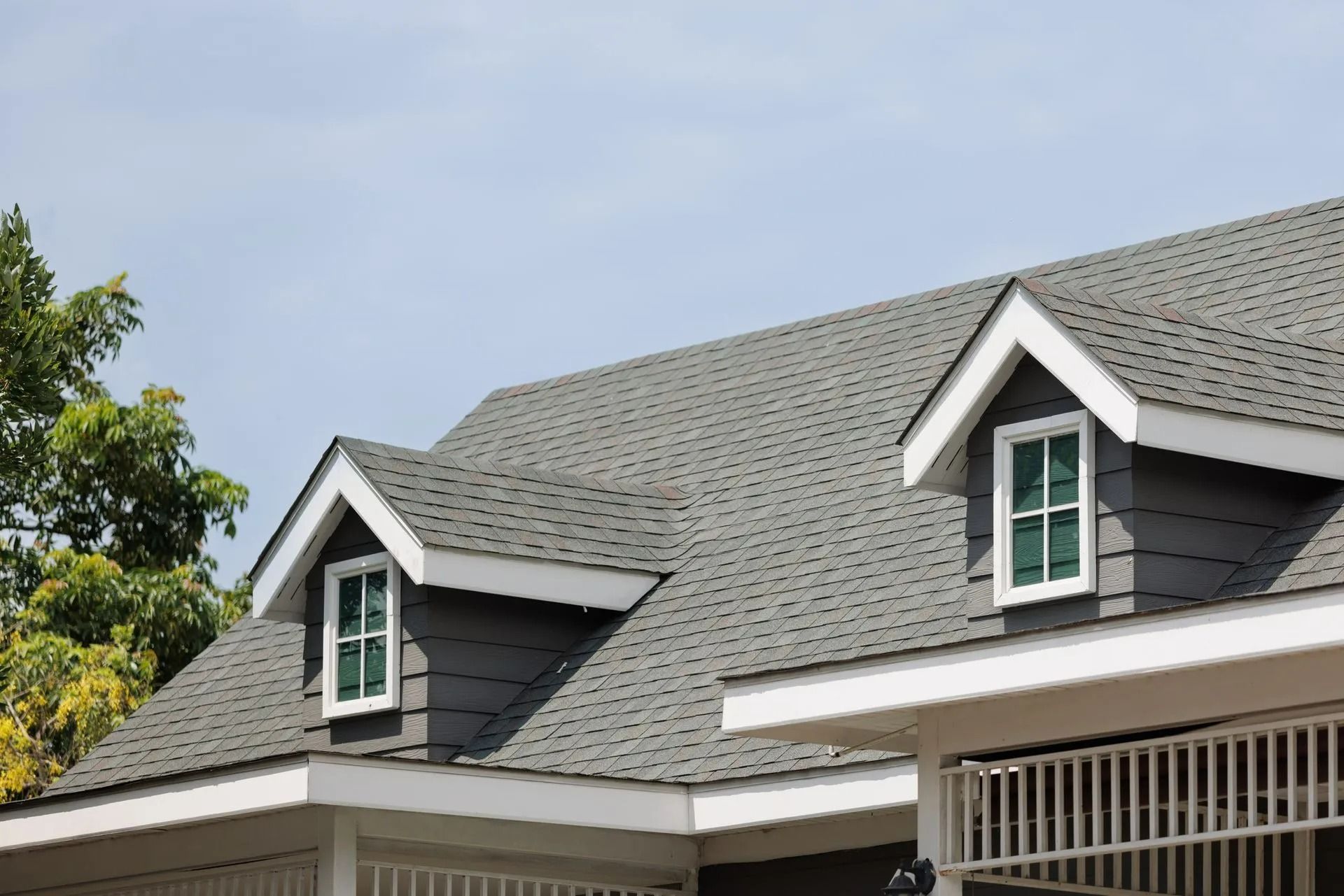 Gray shingle roof with two dormers with white trim and windows. Set against a light blue sky.