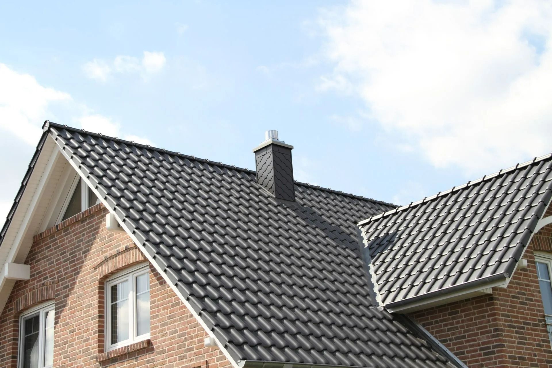 Brick house with a dark tiled roof and chimney against a blue sky with scattered clouds.
