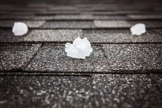 Hailstones on a textured, asphalt shingle roof. The ice appears irregular, with one centered.