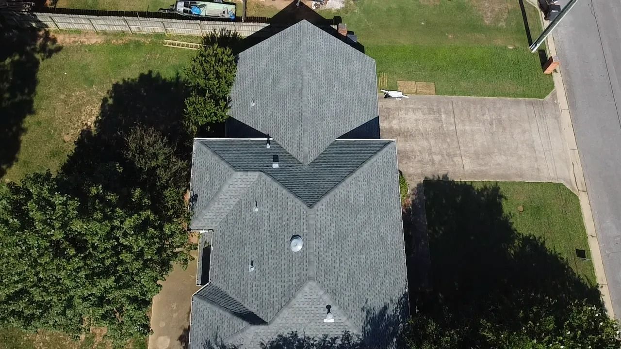 Overhead view of a house with a gray roof, a driveway, and green grass.