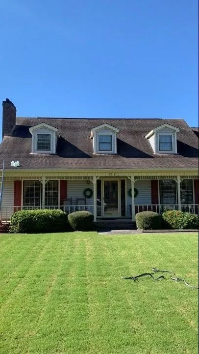 A house with a green lawn, red shutters, and three dormer windows. The sky is blue.