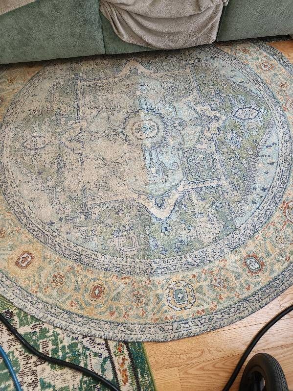 Round, faded rug with blue, beige, and green patterns sits under a green couch.