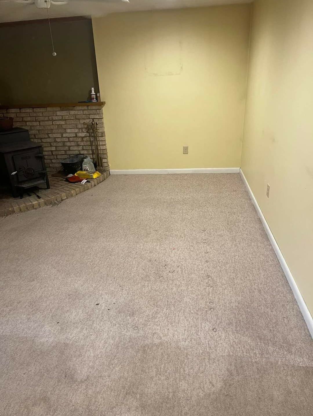 Beige carpeted room with fireplace on left and yellow walls.