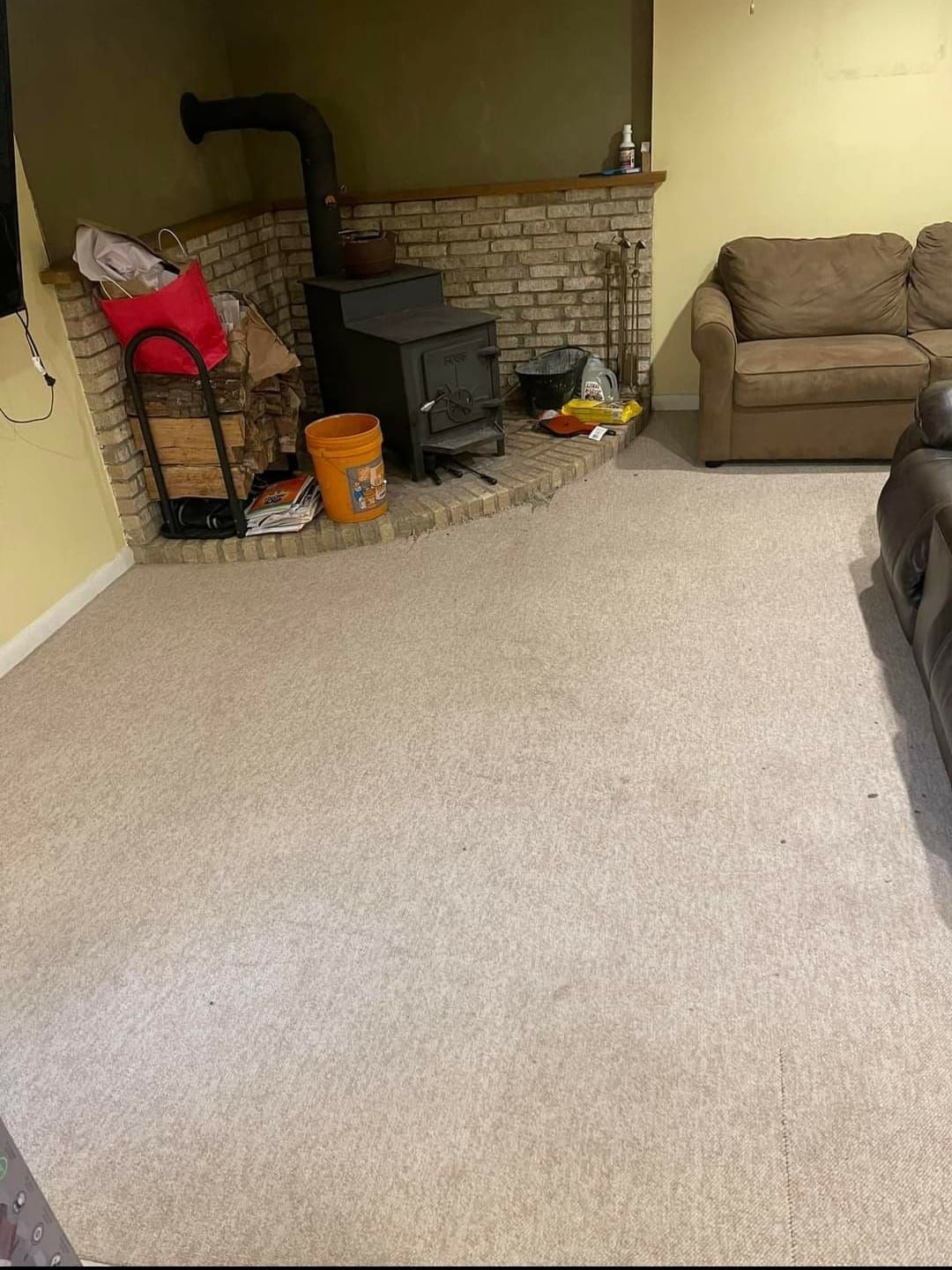 A wood-burning stove sits in a corner with a beige stone facade, beige carpet, and a brown sofa.