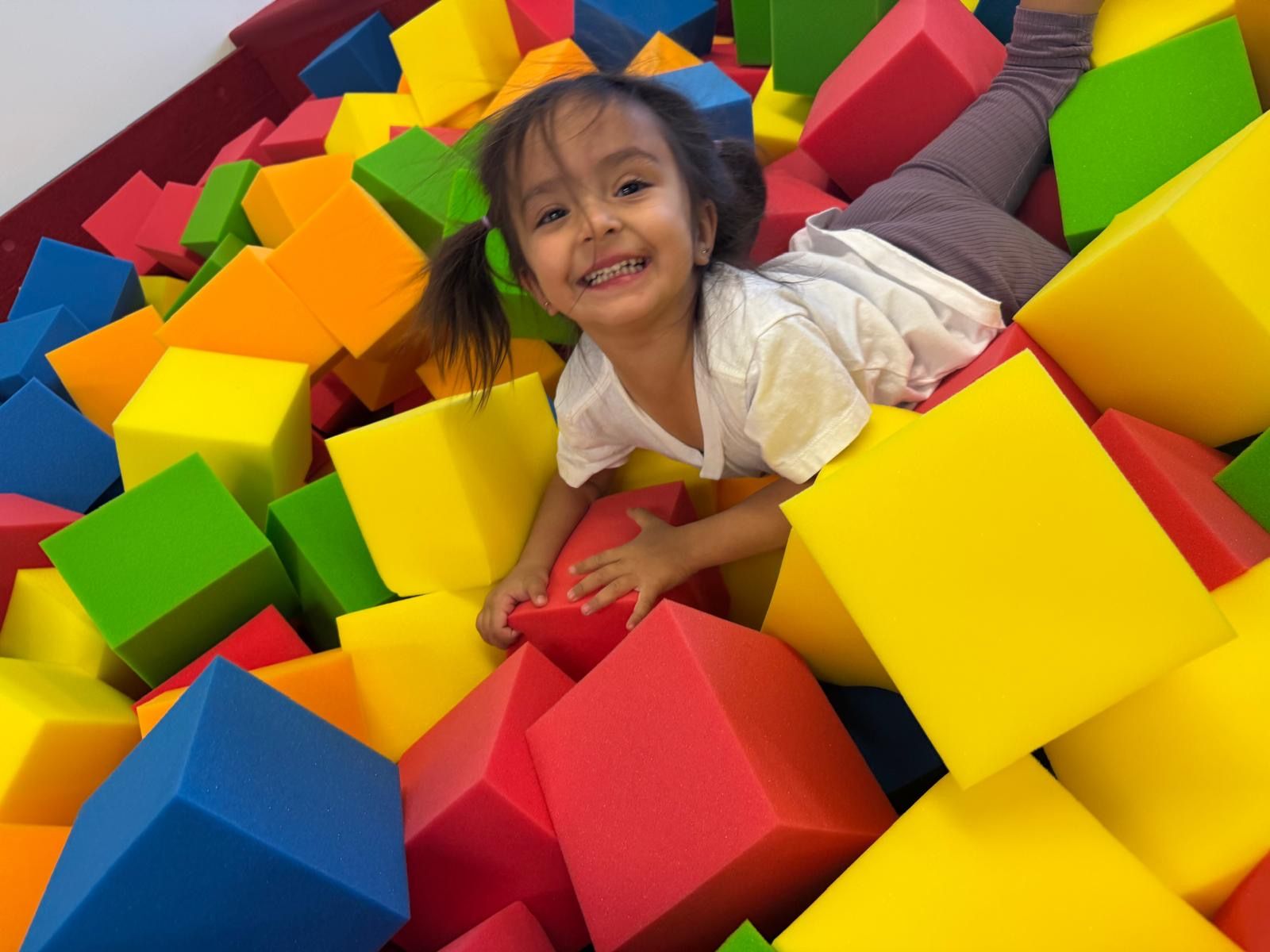Girl in a white shirt and green pants doing the splits on a blue and red mat in a gym.