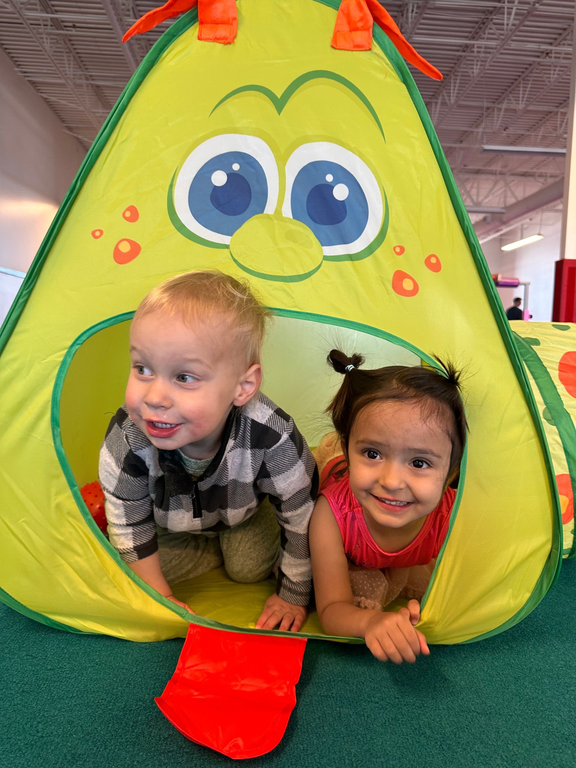 Girl upside down, holding aerial silks, smiling. Colorful toy buildings in background.