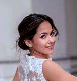 Woman with dark hair in updo smiles, wearing a white lace top.