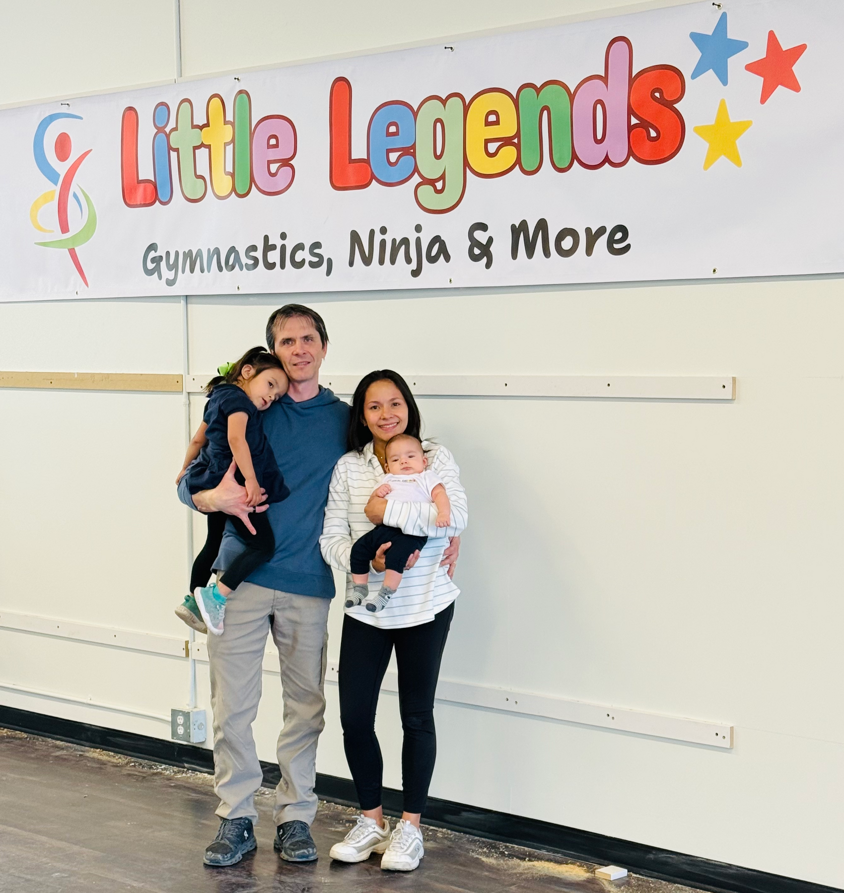 Family and dog sit on a blanket in a park; sunny background.