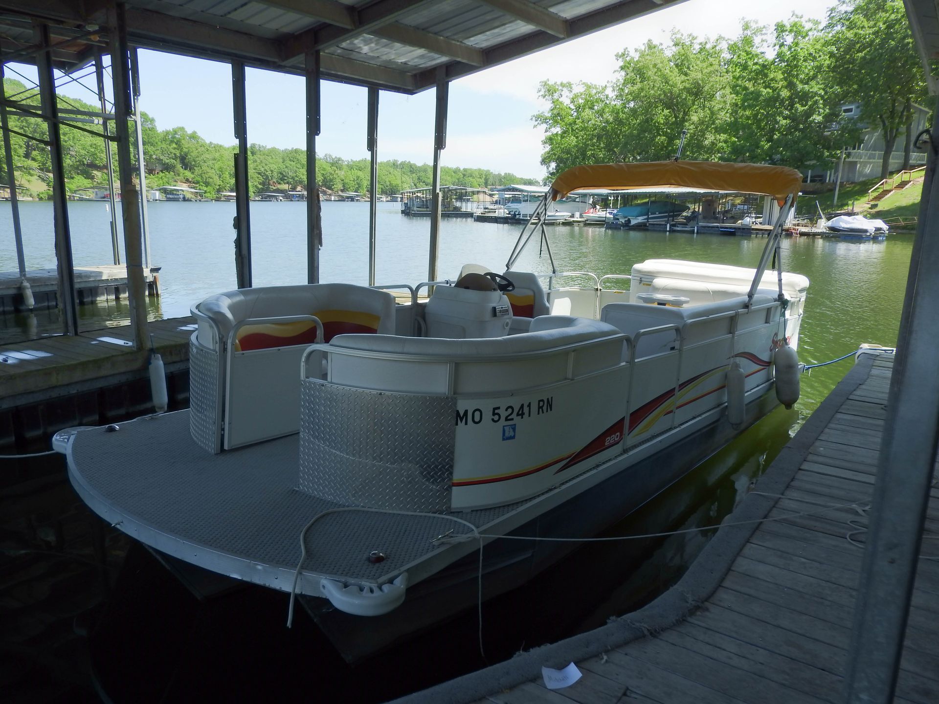 A pontoon boat is docked under a covered dock