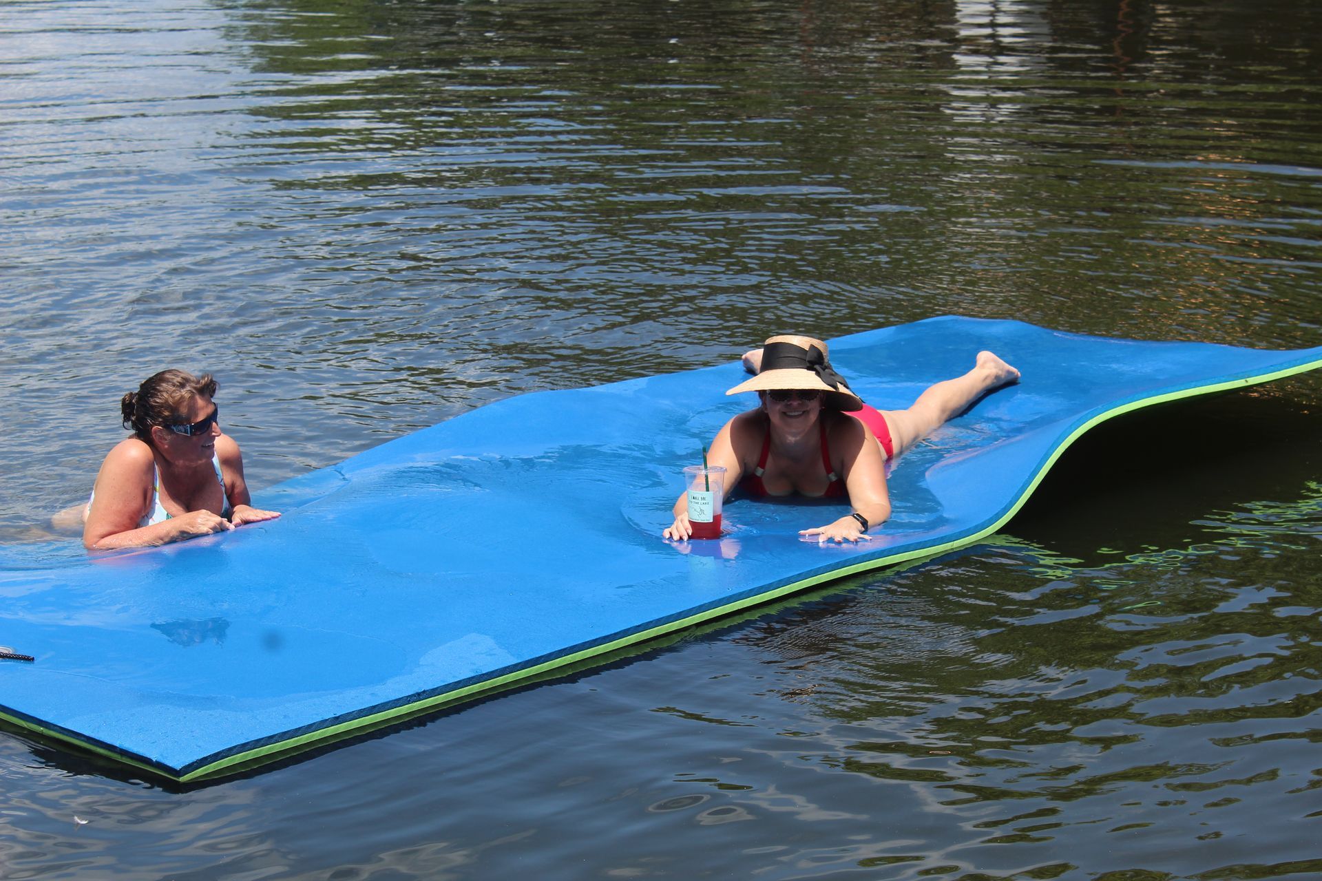 Two women are laying on a blue mat in the water.