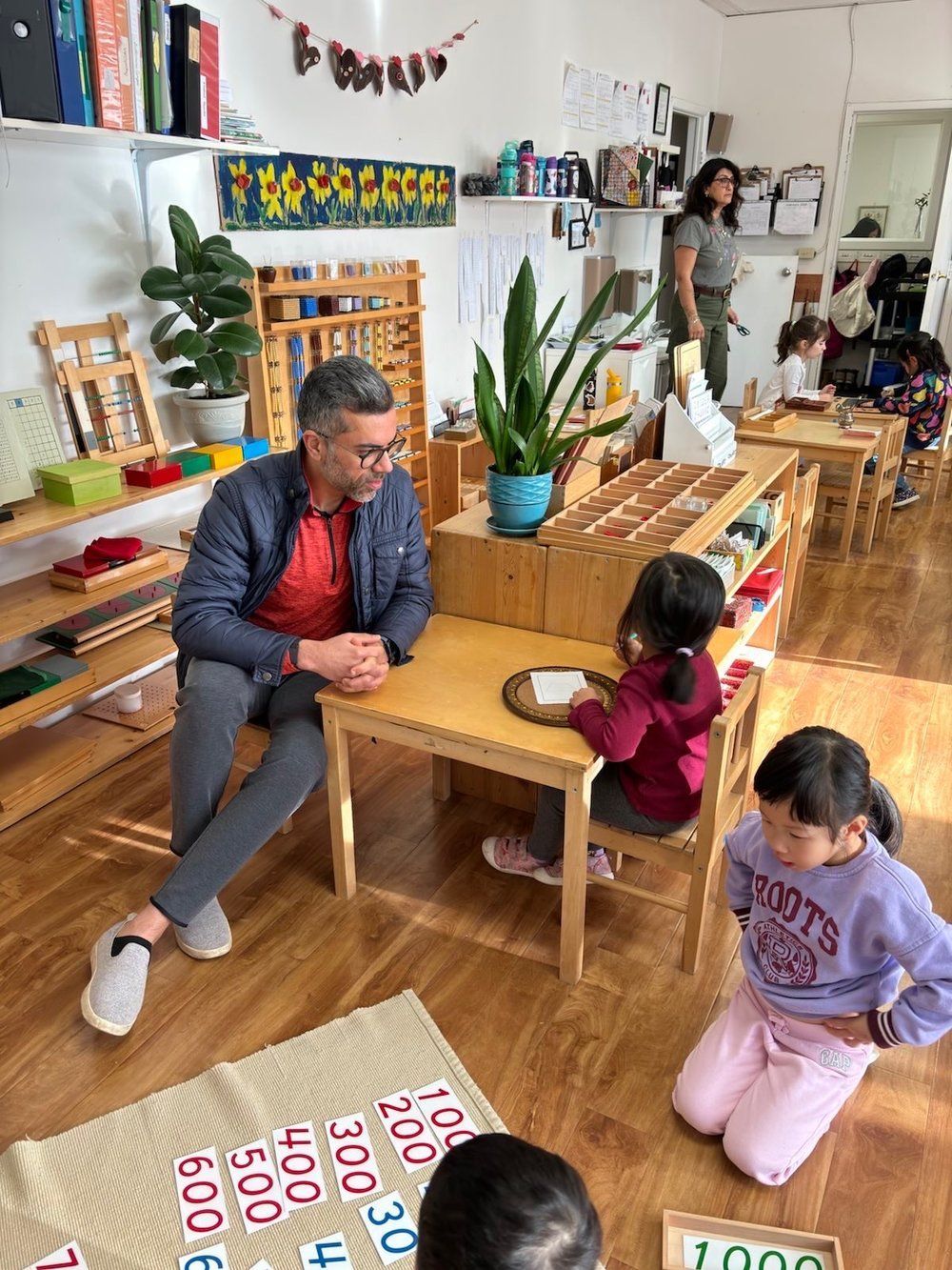 A man is sitting at a table in a classroom with children.