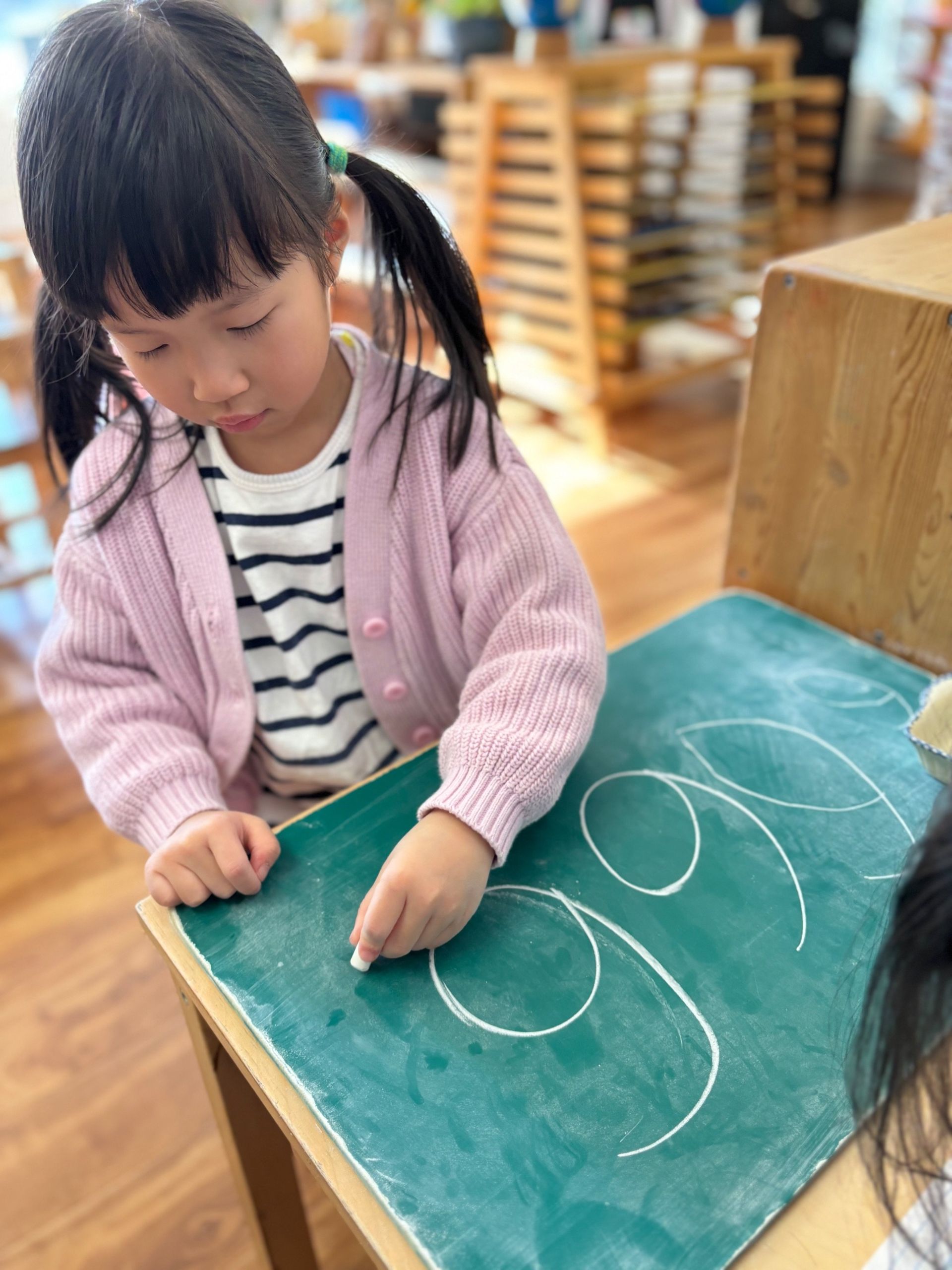 A little girl is writing on a blackboard with chalk