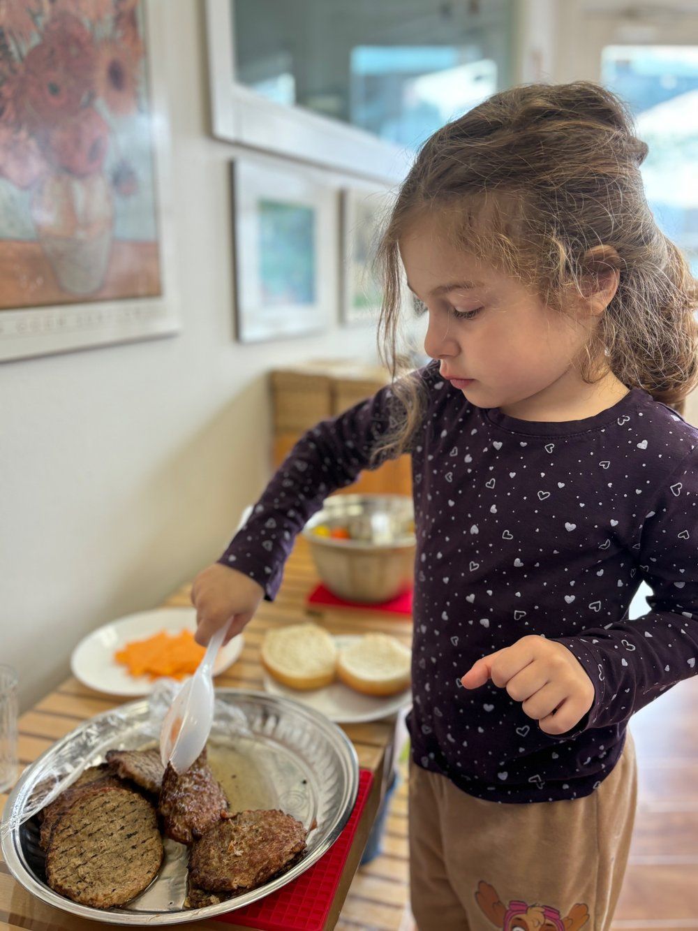 A little girl is holding a spoon over a pan of food.