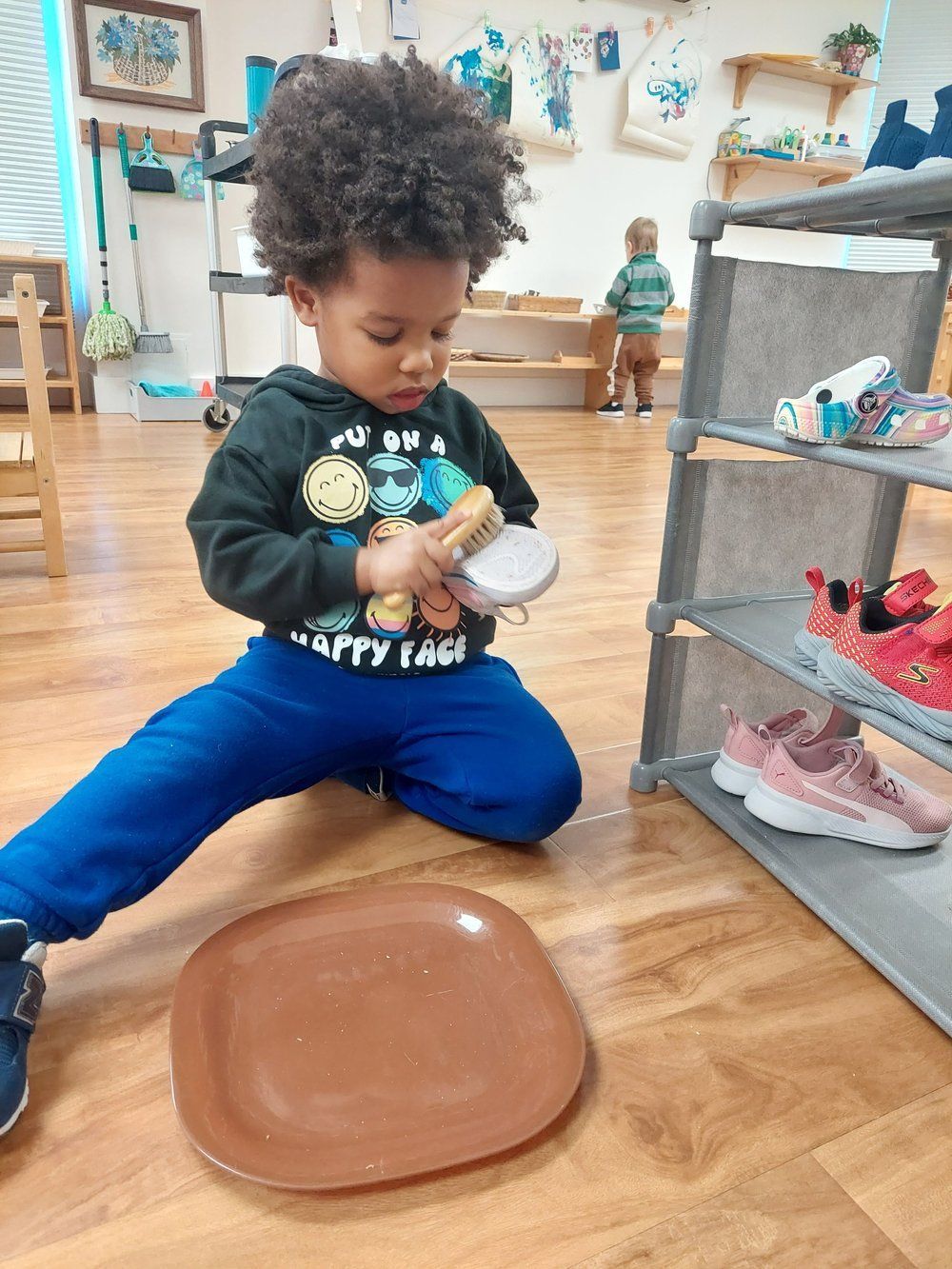 A young boy is kneeling on the floor playing with a spoon and a plate.