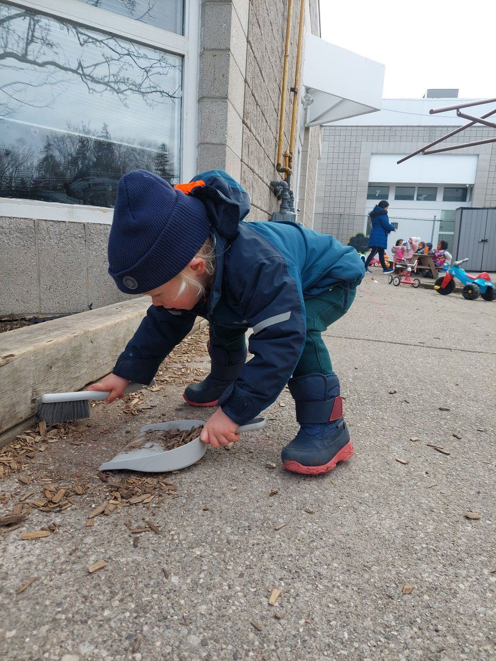 A young boy is cleaning the sidewalk with a shovel.