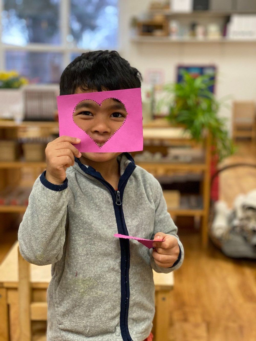 A young boy is holding a piece of paper with a heart on it in front of his face.