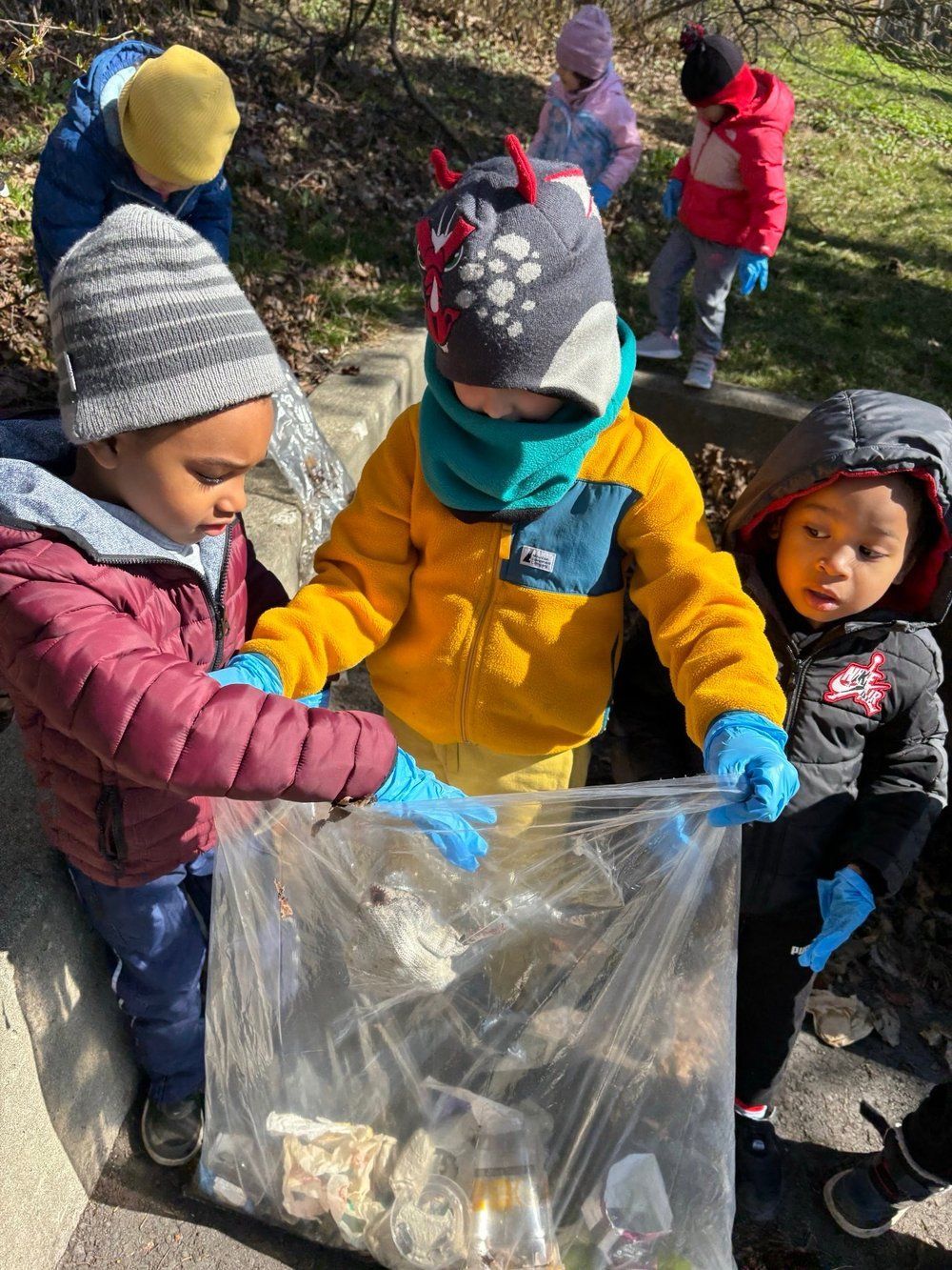 A group of children are gathering trash in a plastic bag.