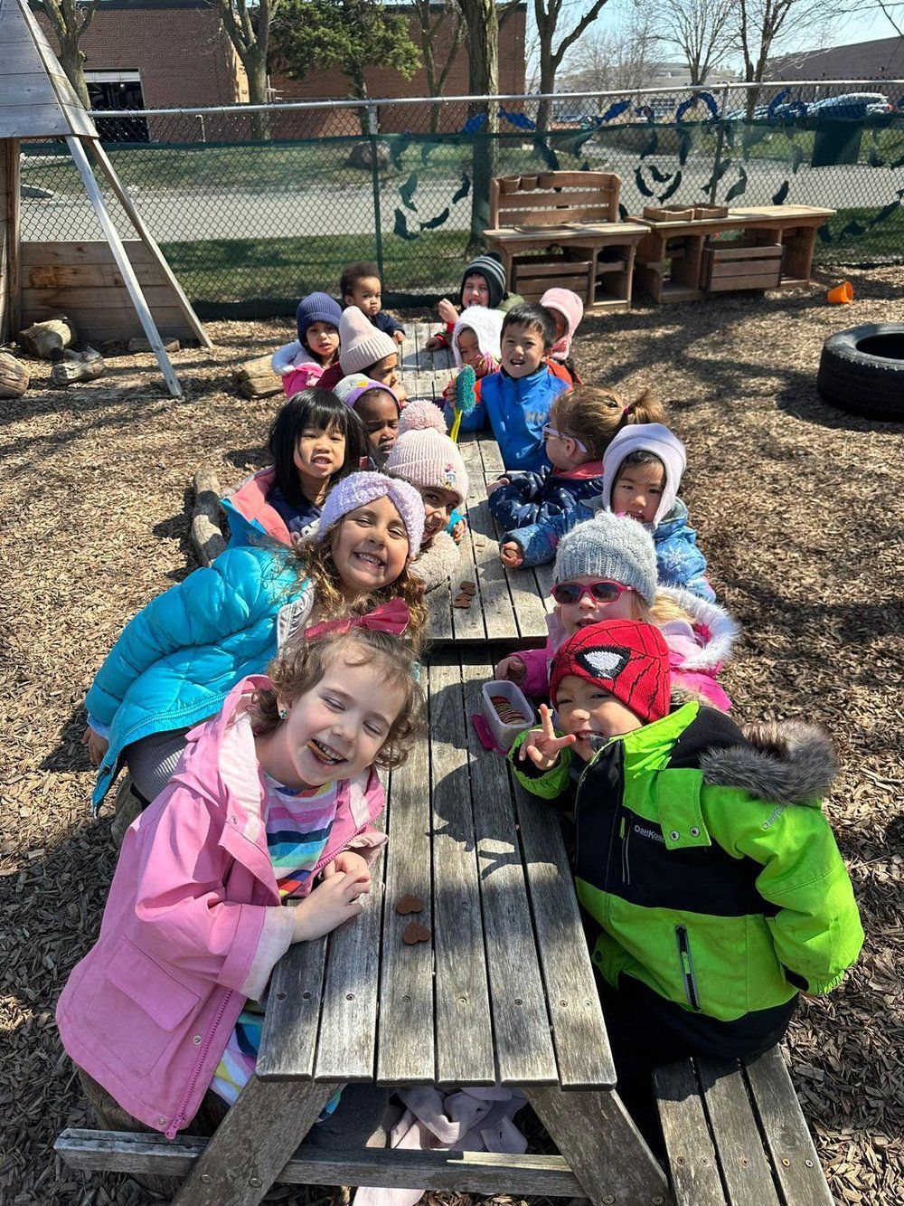 A group of children are sitting at a picnic table in a park.