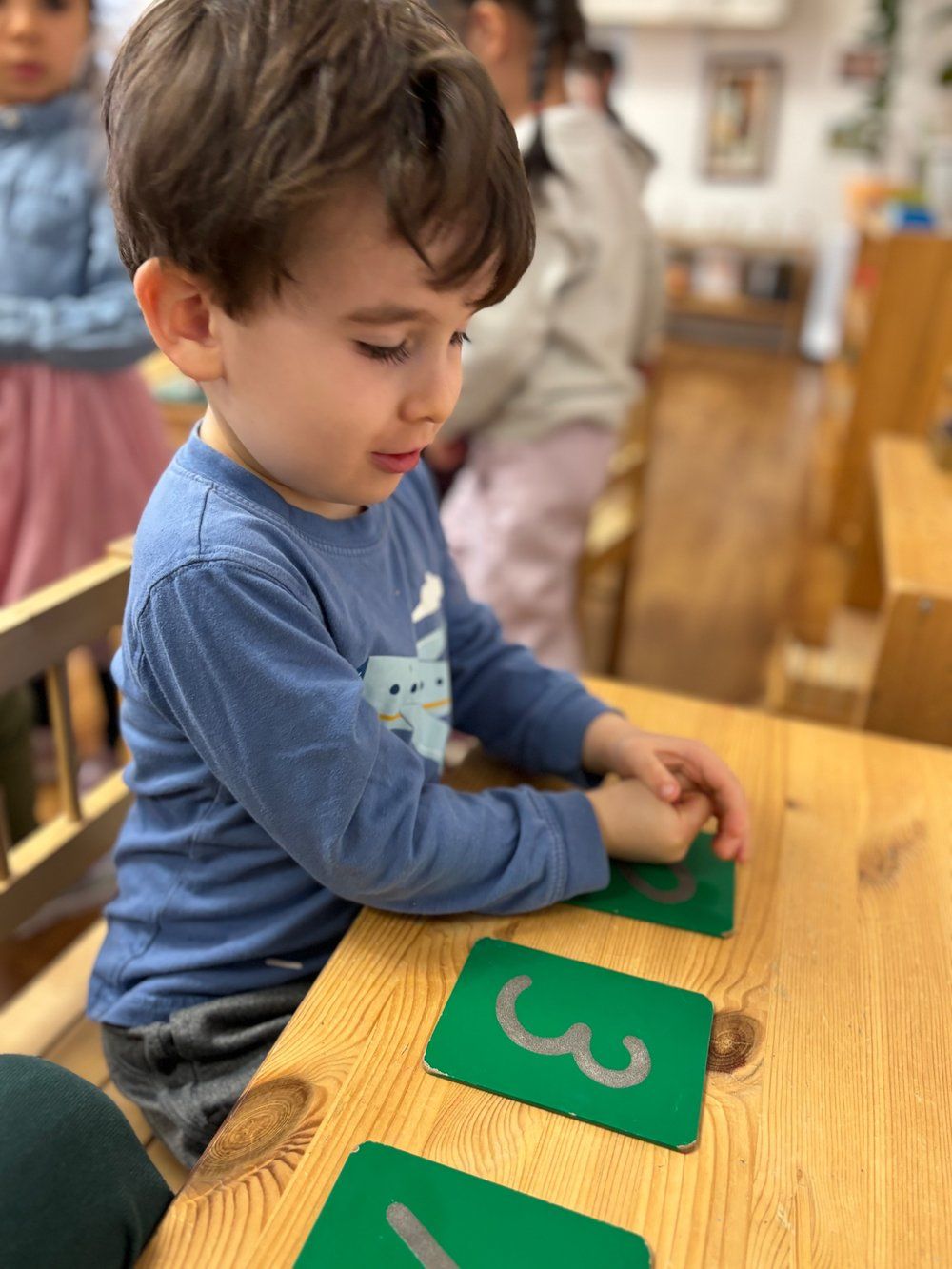 A young boy is sitting at a wooden table playing with numbers on green cards.