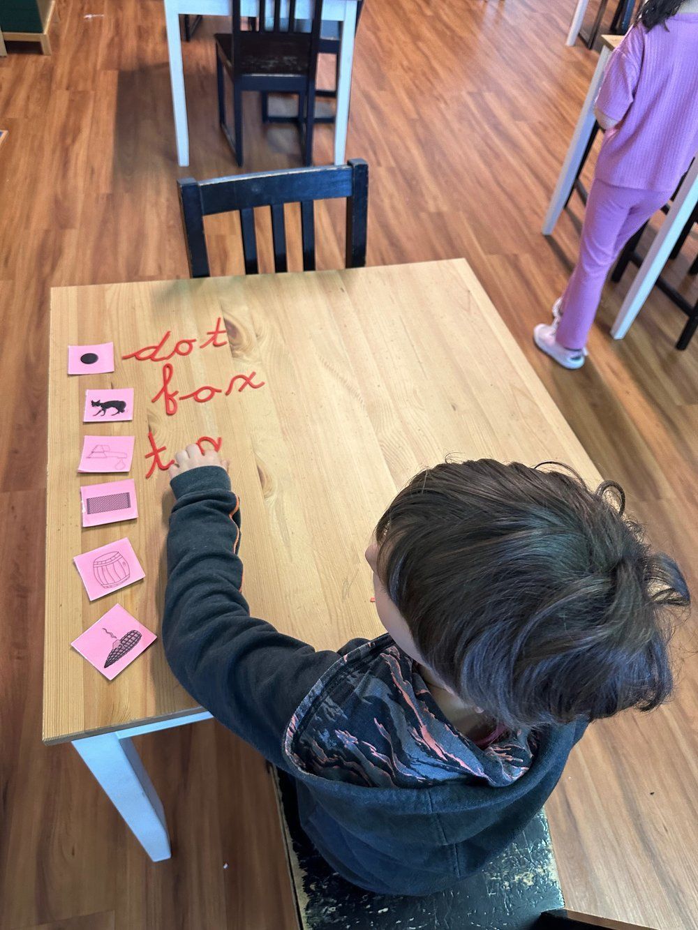A young boy sits at a wooden table writing on it