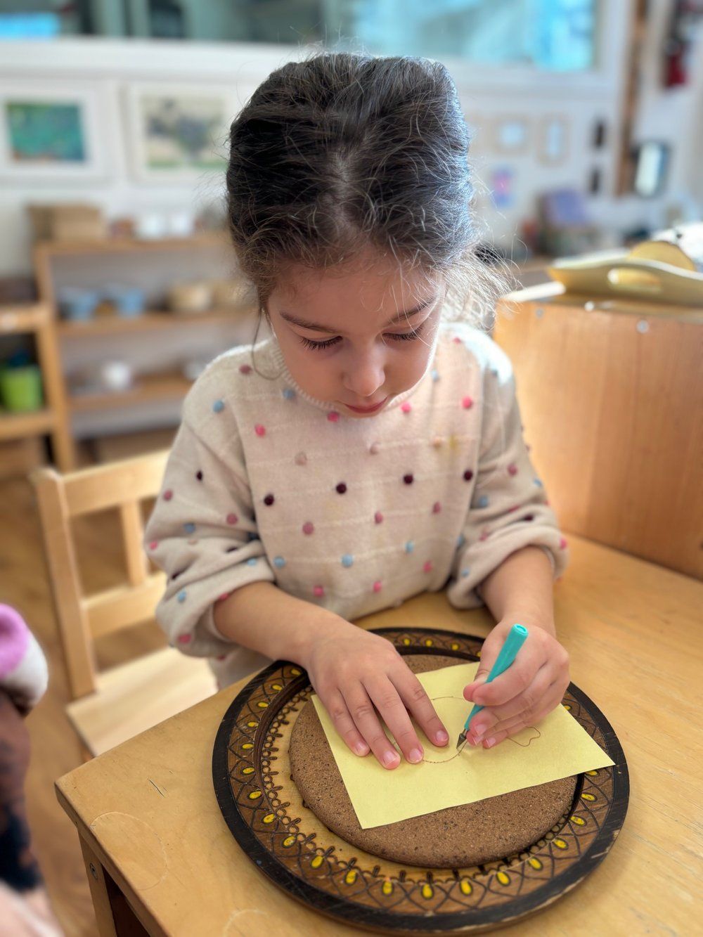 A little girl is sitting at a table writing on a piece of paper.