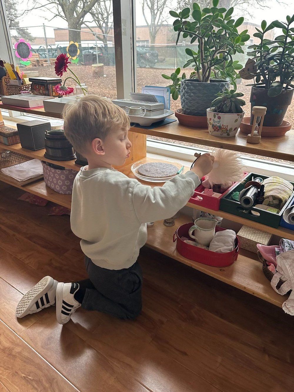 A young boy is kneeling down in front of a shelf with potted plants.