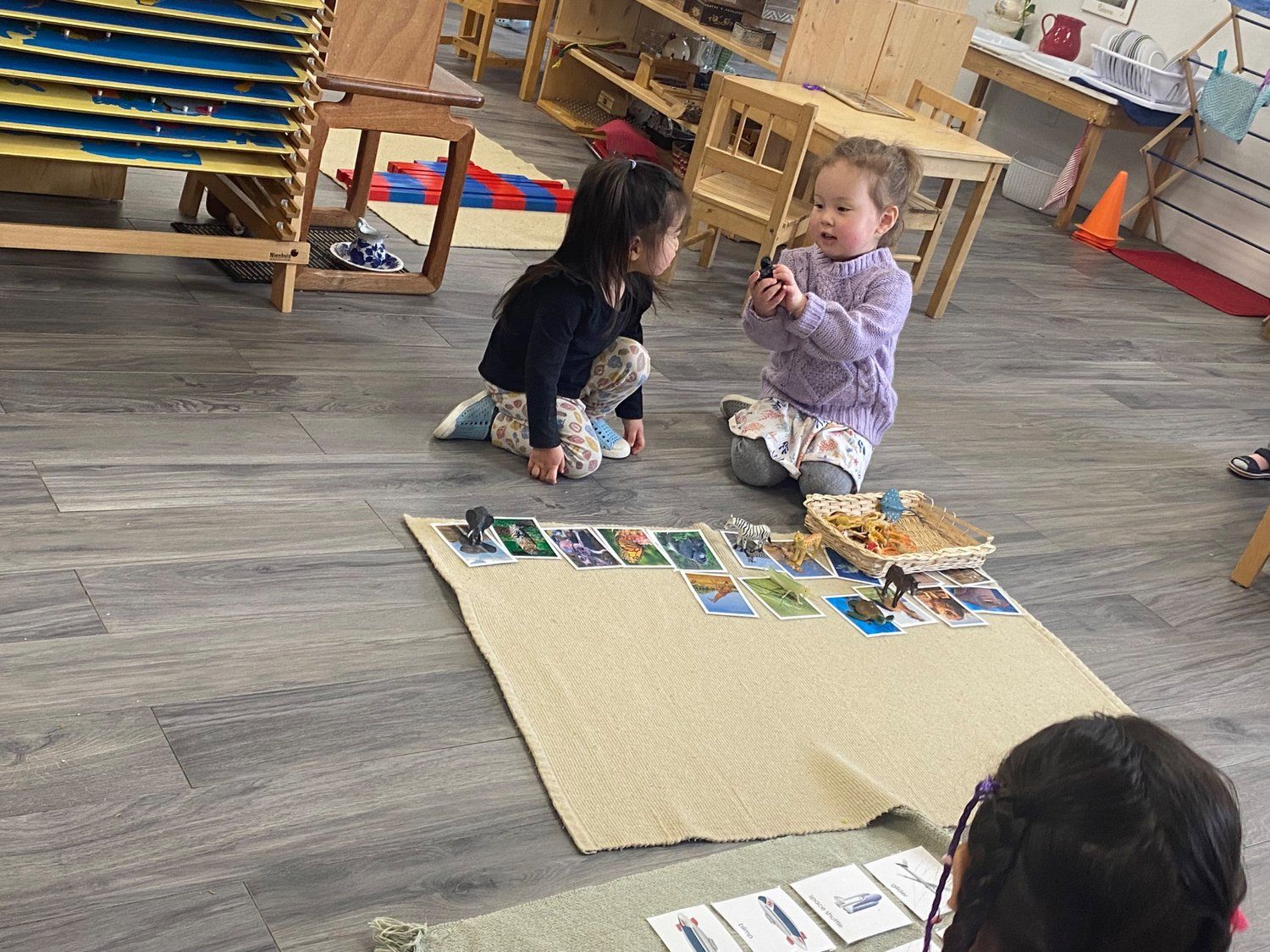 Two little girls are playing with cards on the floor in a classroom.
