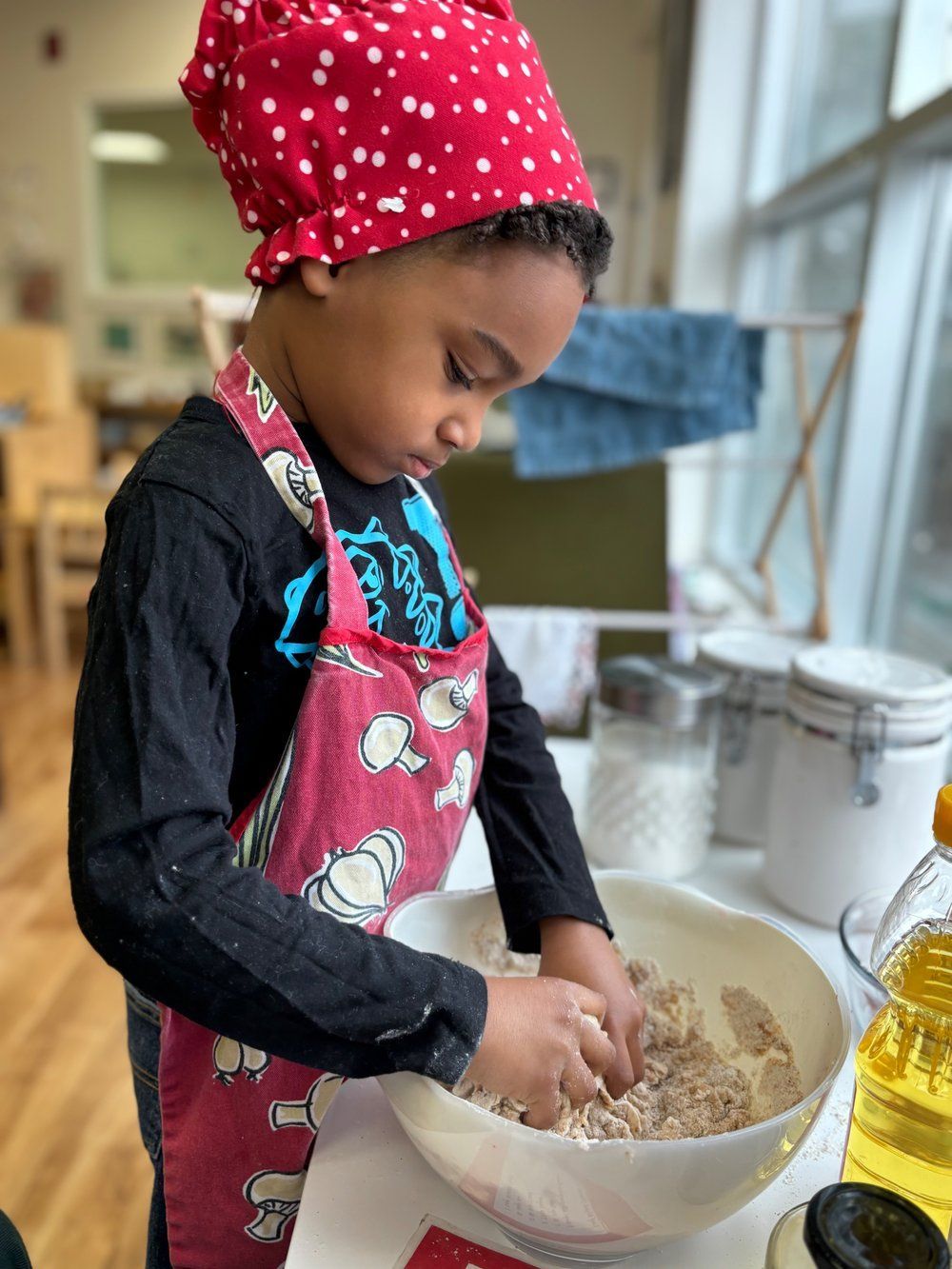 A young boy wearing a red hat and apron is mixing ingredients in a bowl.