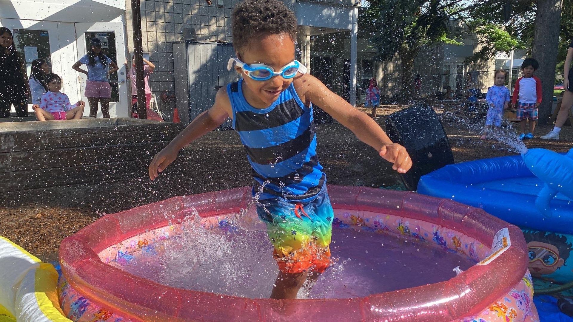 A young boy wearing goggles is jumping into an inflatable pool.