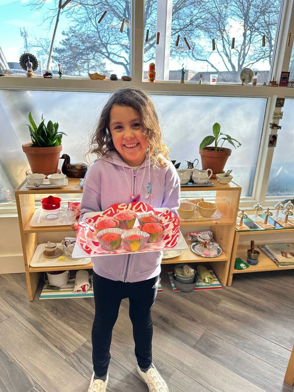 A little girl is holding a plate of cupcakes in a room.