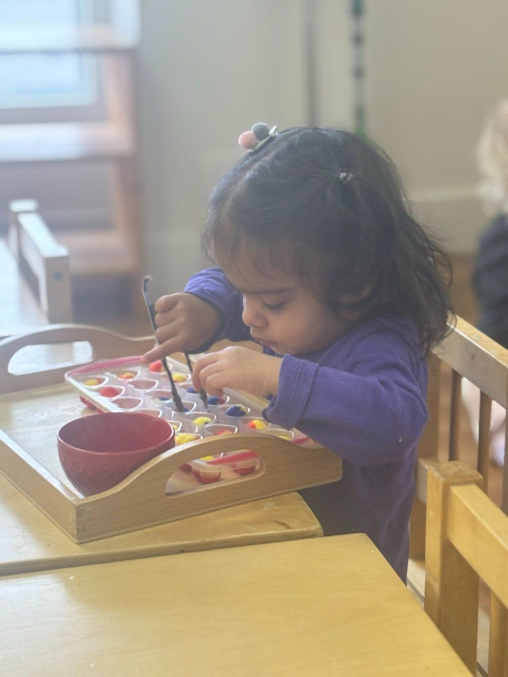 A little girl is sitting at a table painting with a brush.