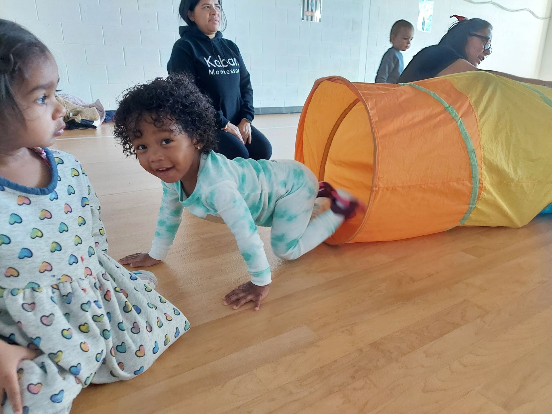 A little girl is crawling through a tunnel on the floor.