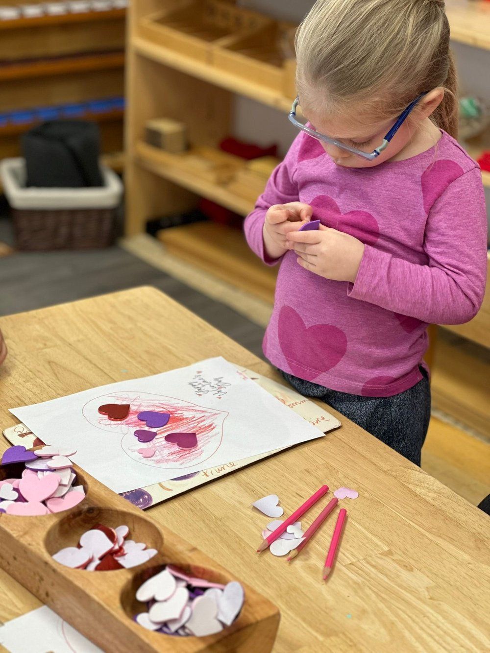 A little girl wearing glasses is sitting at a table playing with hearts.