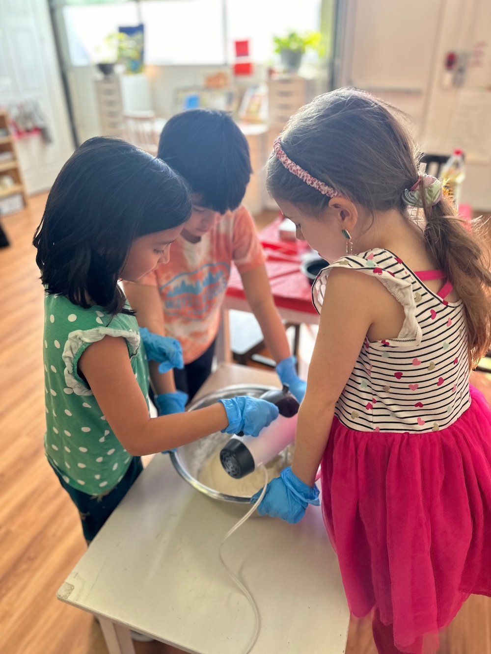 Three young girls are standing around a table mixing ingredients in a bowl.